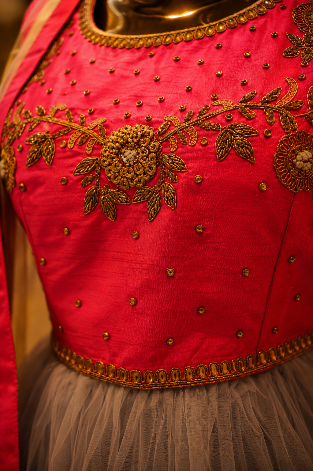 Close-up of a bright pink traditional blouse with intricate gold embroidery, beadwork, and a sheer gray tulle skirt.